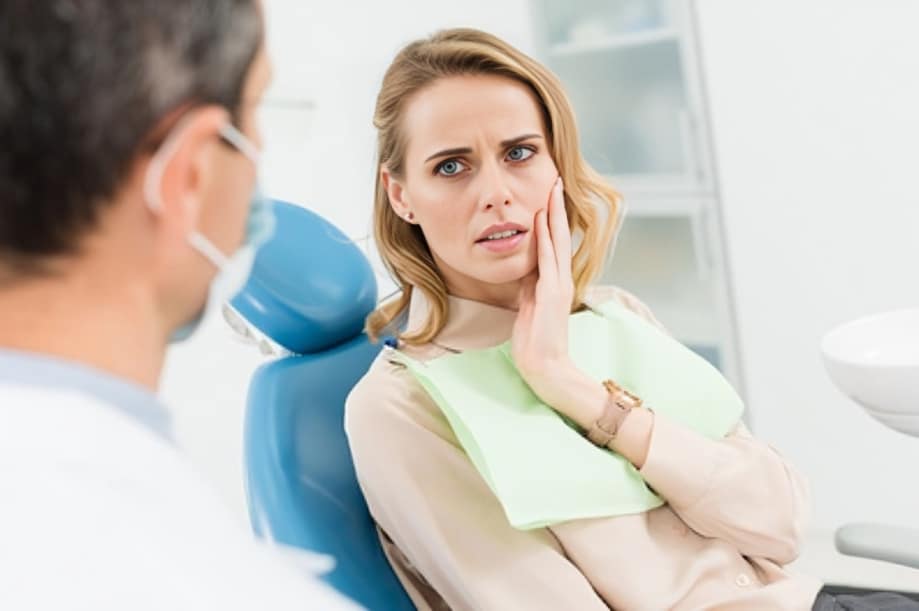 Woman patient in dental chair touching face during examination at Uptown Dental Associates office.