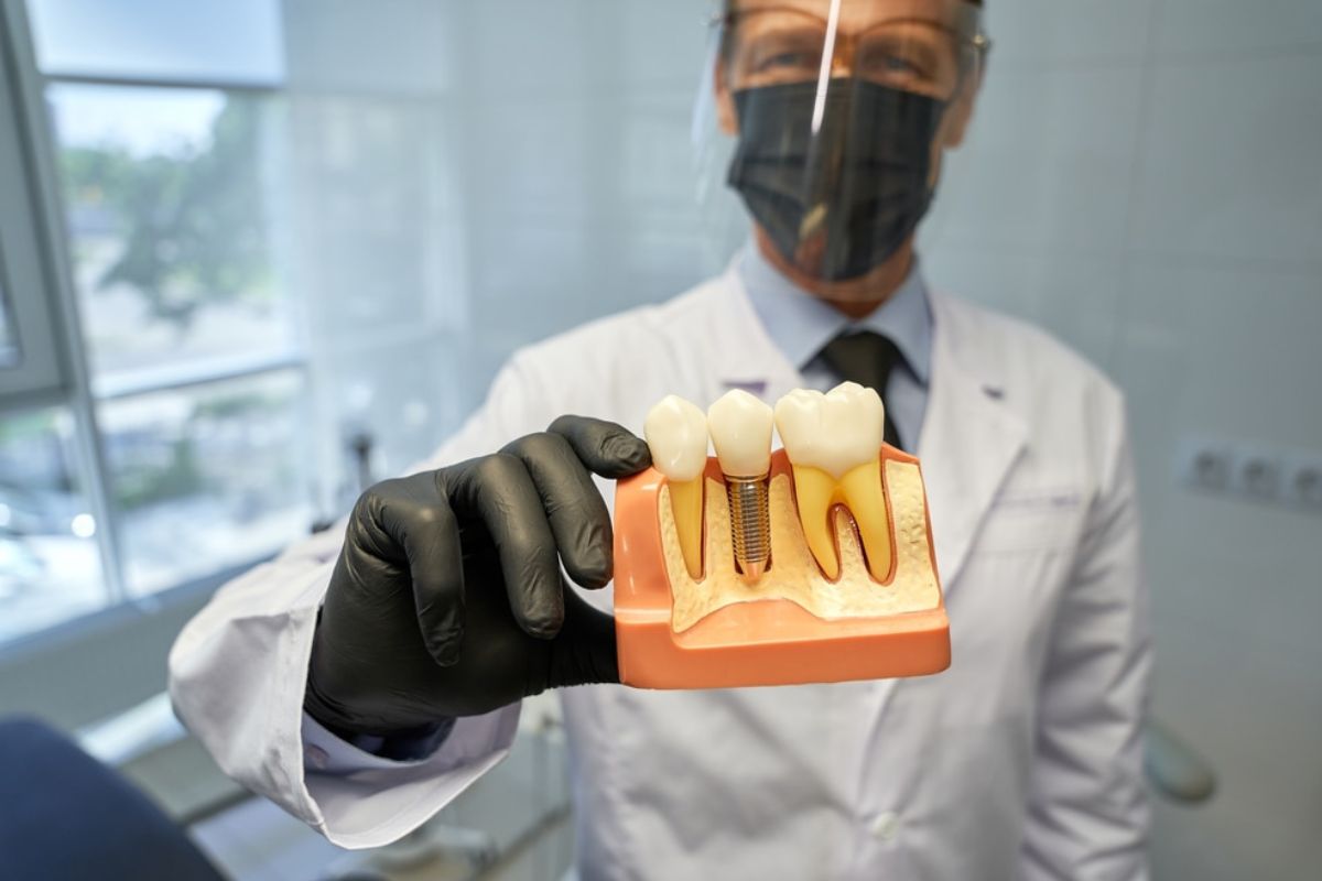 Dentist in white coat and mask holding illuminated dental model in modern office setting.